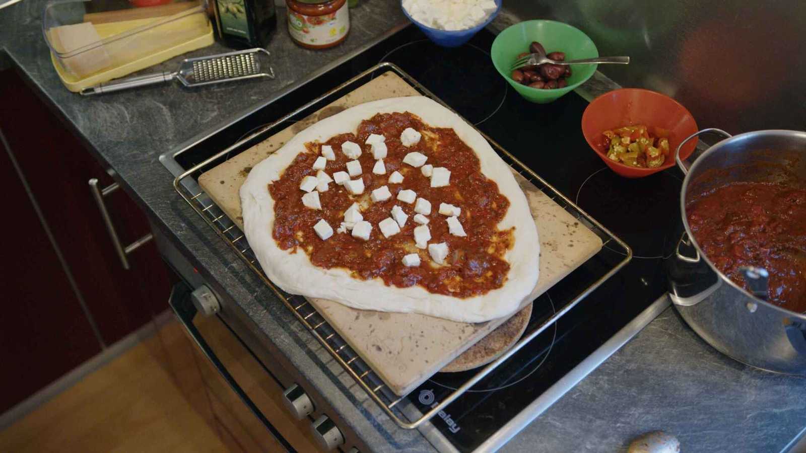 Pizza dough on stone with tomato sauce and mozzarella