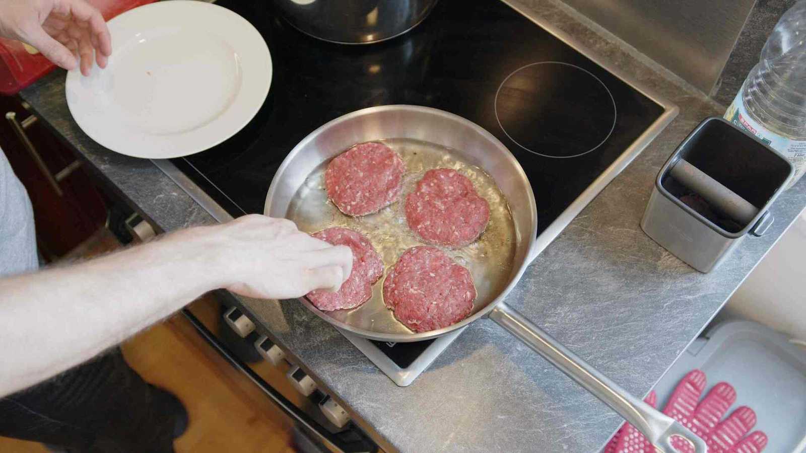 Raw patties in a pan being cooked